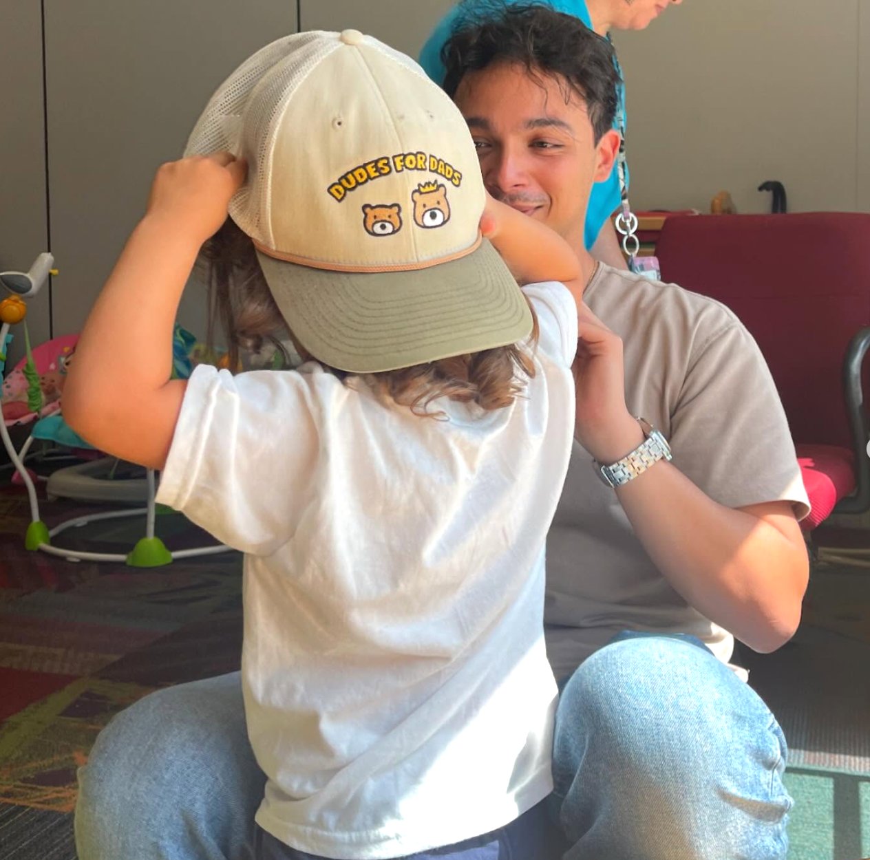 A child putting on a Dudes For Dads cap with a mentor smiling behind them